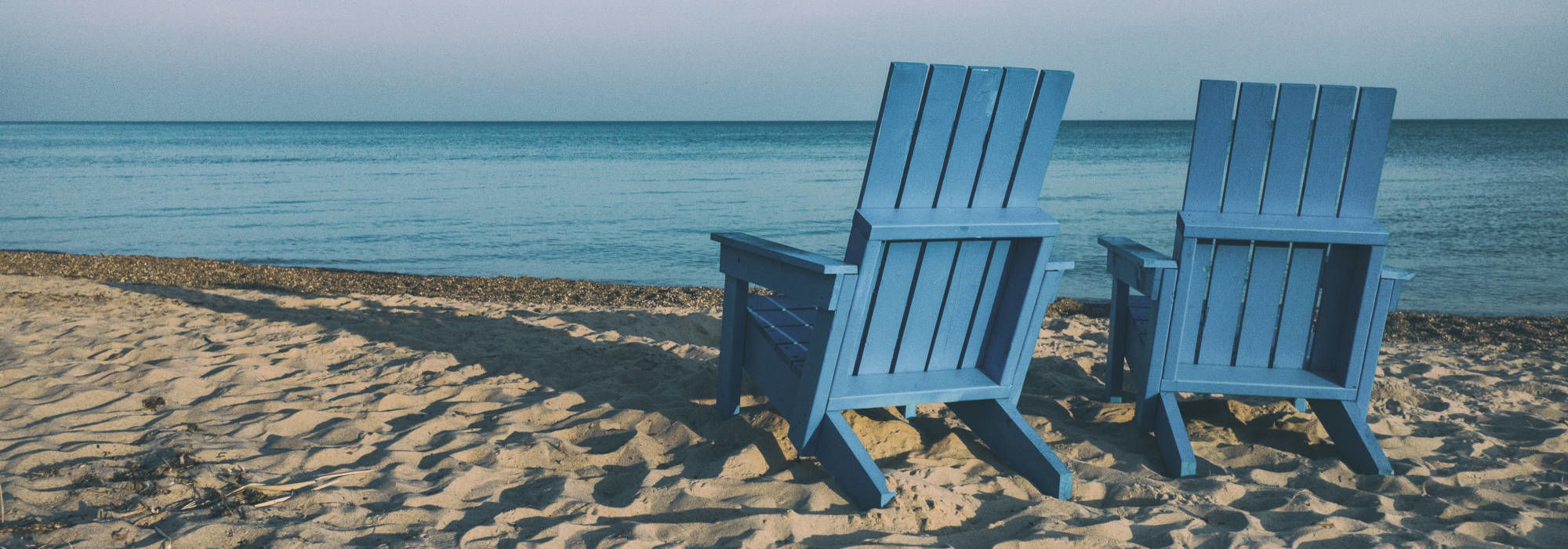 Δύο μπλε καρέκλες στην αμμουδιά δίπλα στη θάλασσα.